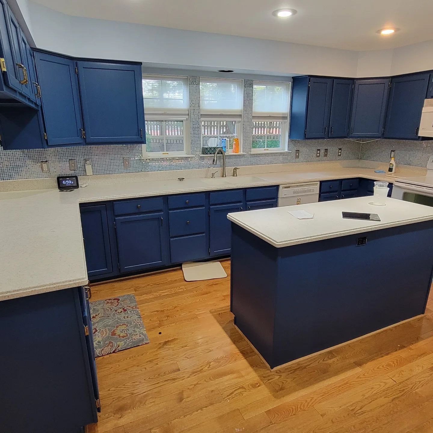 Blue kitchen with white countertops, island, wood floor, and window over the sink