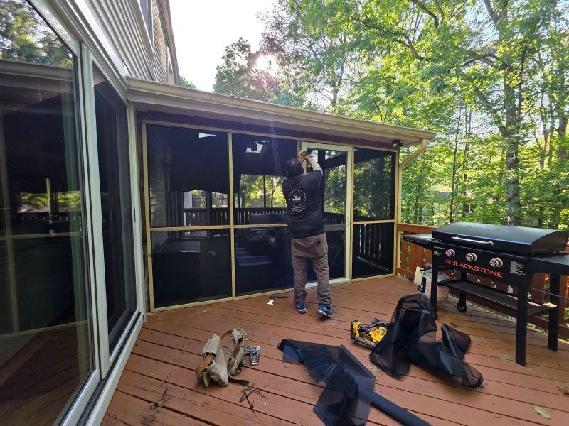 Person painting a screened porch ceiling beside a grill, with tools and gear on the deck