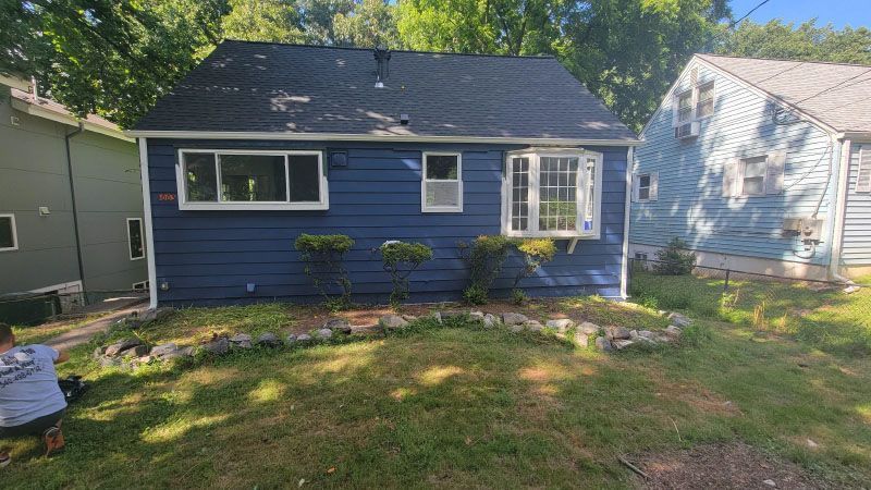 Blue single-story house with white trim and a small front lawn, framed by neighboring homes and trees.