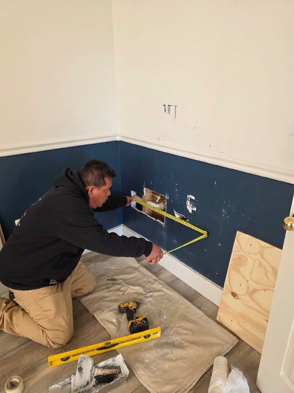 Worker measuring a wall with a tape in a partially renovated room with blue paneling and tools on the floor