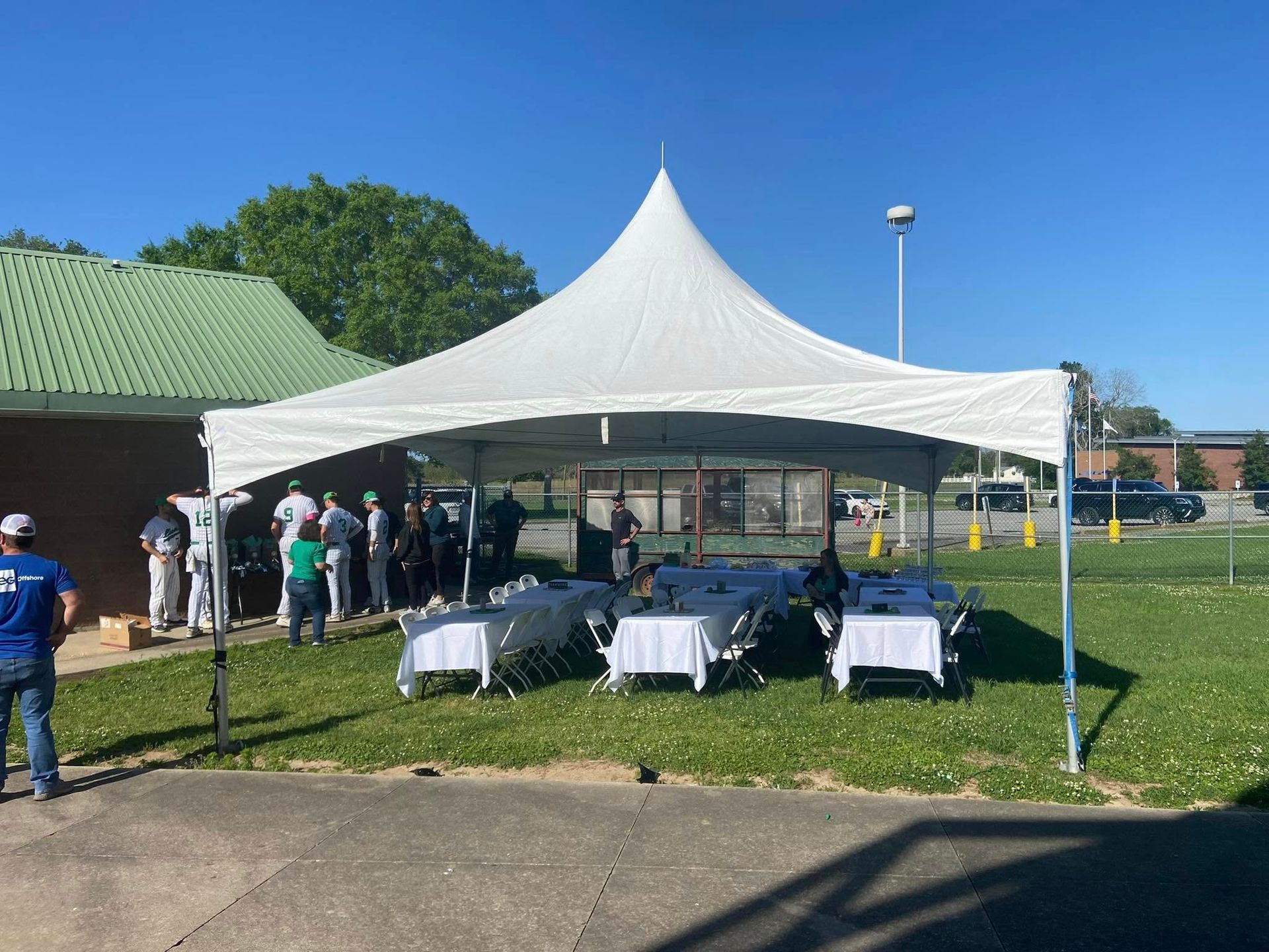 White event tent with tables set up outdoors on a sunny day, with people gathered nearby.