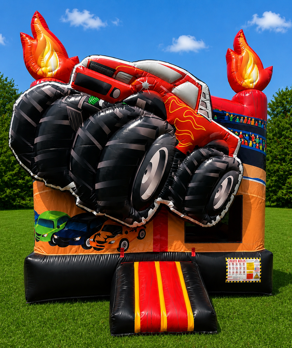 Red monster truck on a colorful inflatable bounce house with flame decorations outdoors on grass.