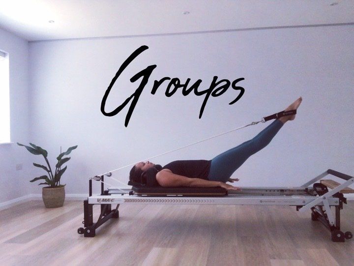 A woman is laying on a pilates machine in front of a wall that says groups
