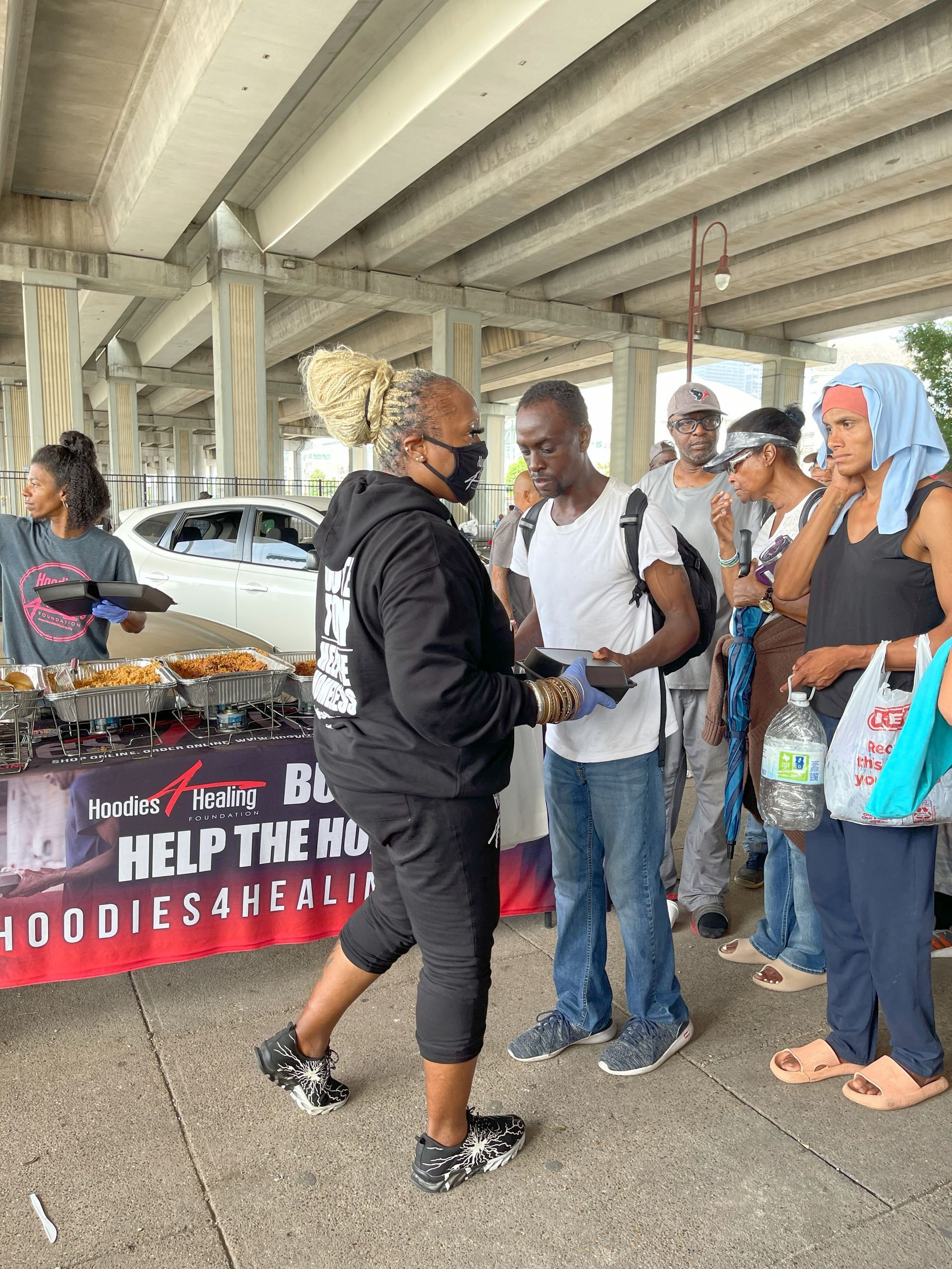 A group of people are standing around a table under a bridge.