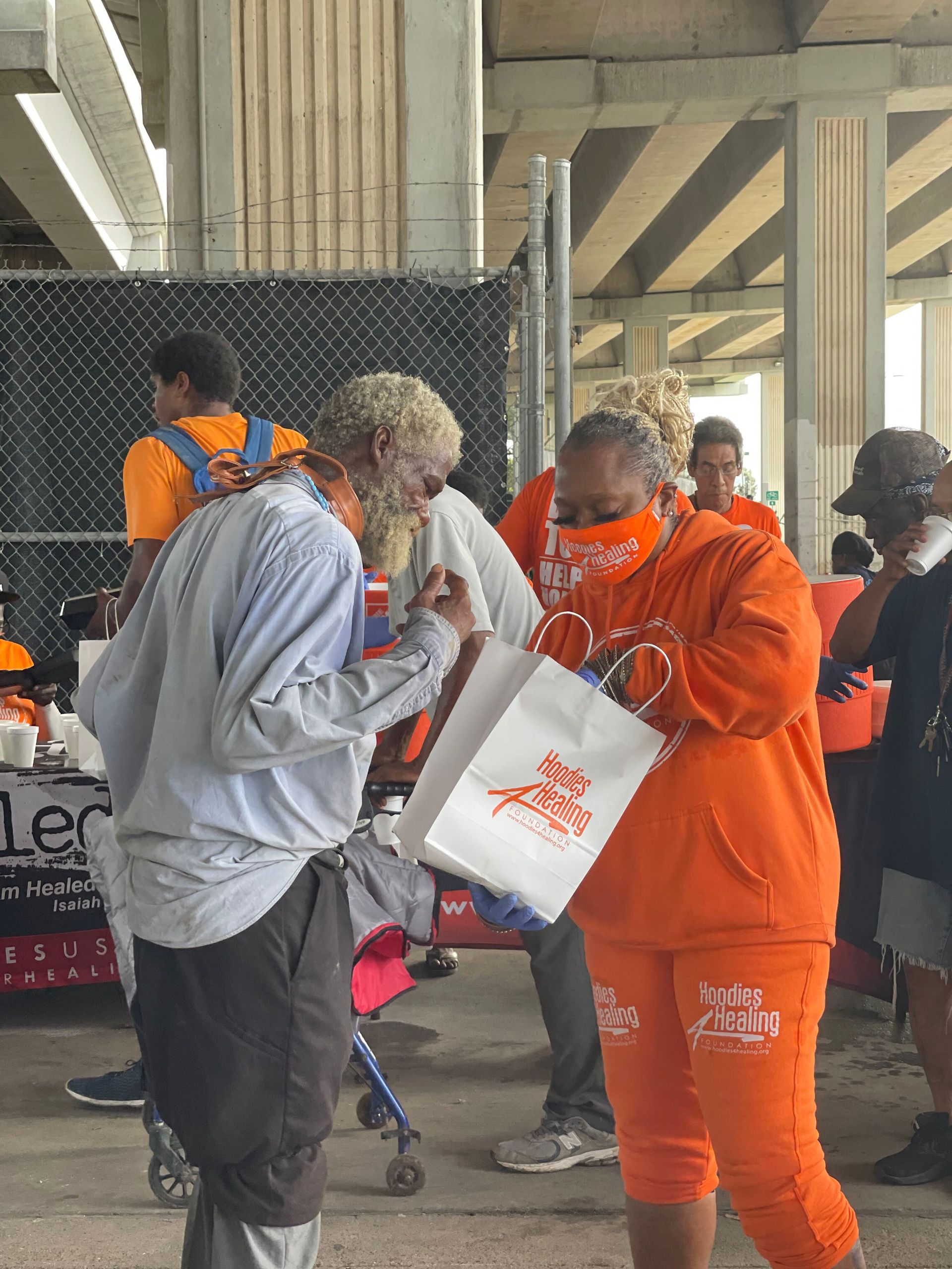 A woman in an orange hoodie is holding a bag and talking to a man.