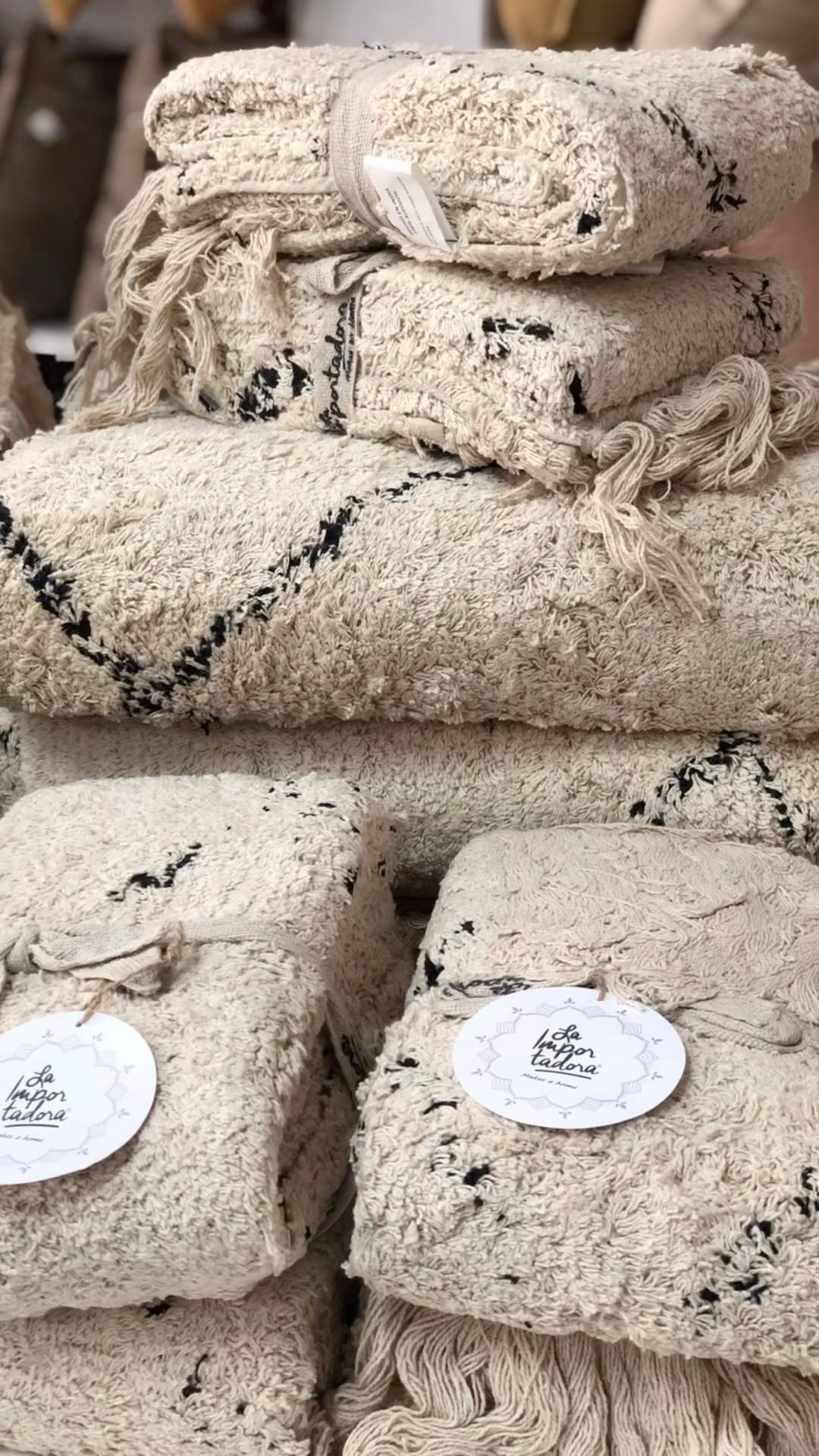 Montones de alfombras texturizadas de color crema con diseños geométricos negros, algunas agrupadas con etiquetas.