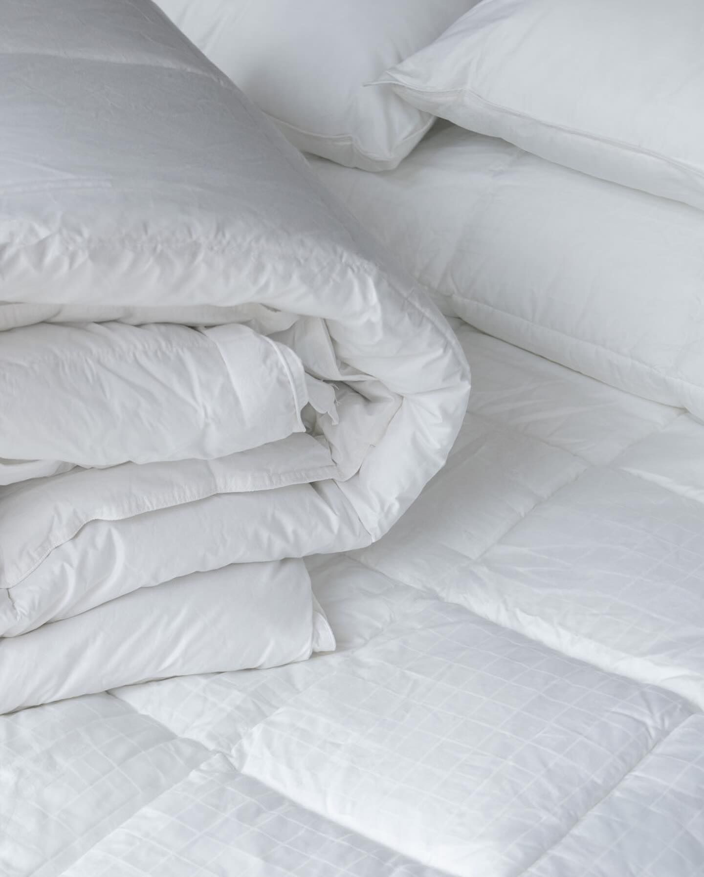 Ropa de cama blanca: un edredón doblado, almohadas y un protector de colchón acolchado.