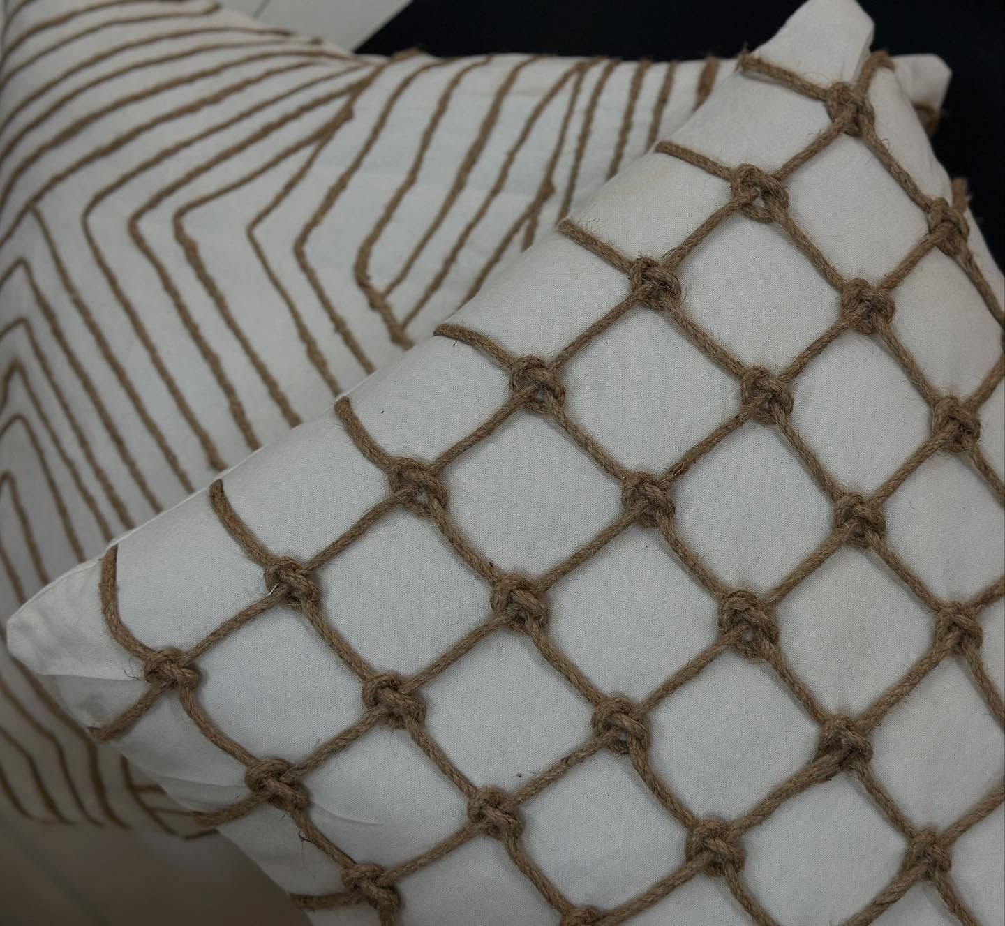 Dos cojines decorativos blancos, uno con detalles marrones en forma de red y el otro con un diseño geométrico marrón.