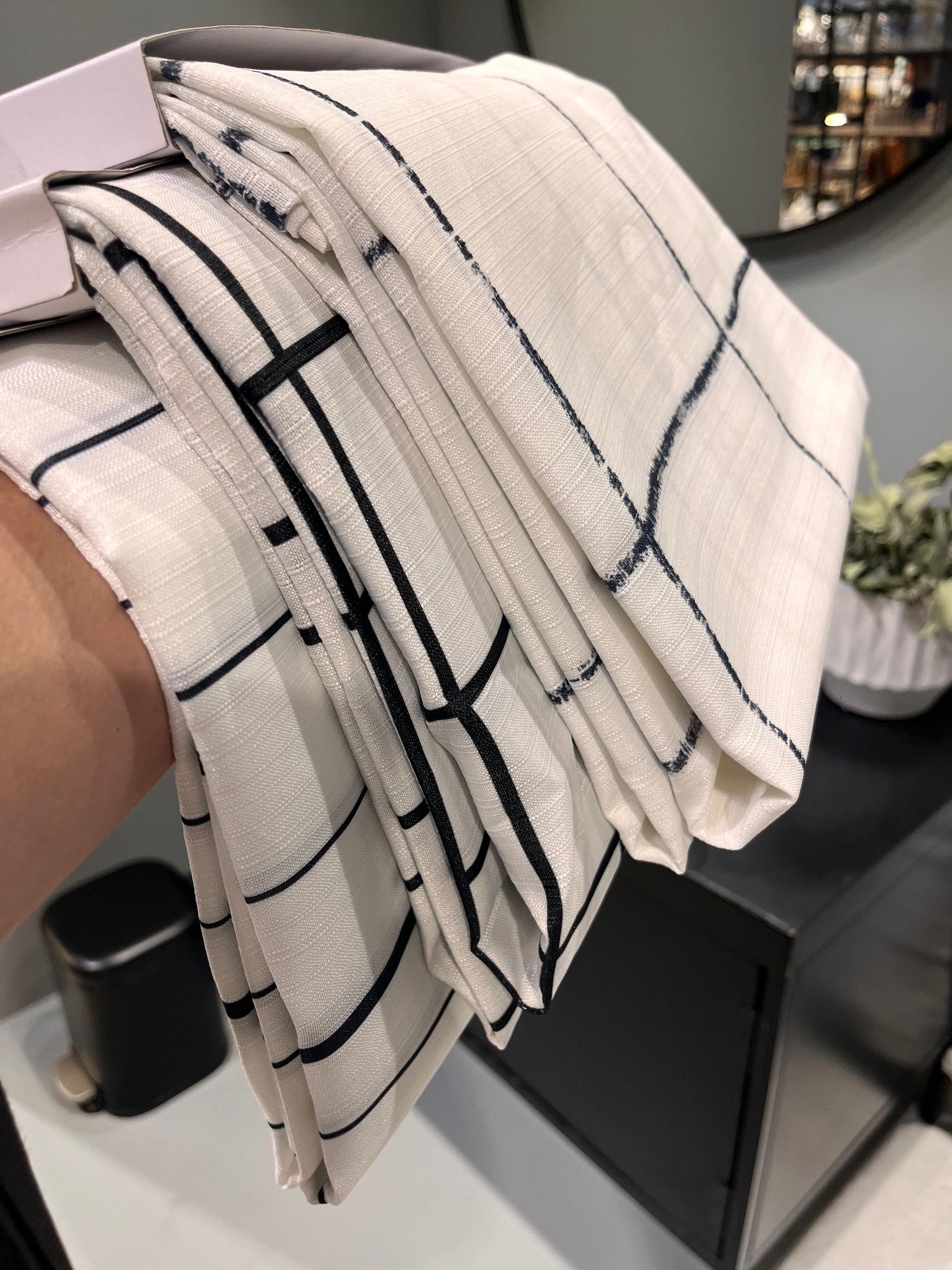 Mano sosteniendo toallas blancas dobladas con un patrón de cuadrícula negra, cerca de una cortina de ducha a juego.