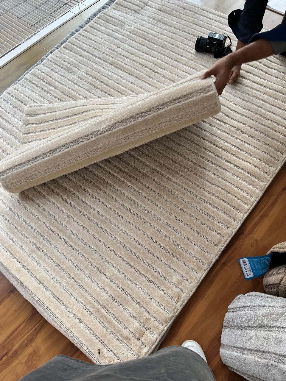 Alfombra beige estampada, parcialmente enrollada, dejando al descubierto la parte inferior.