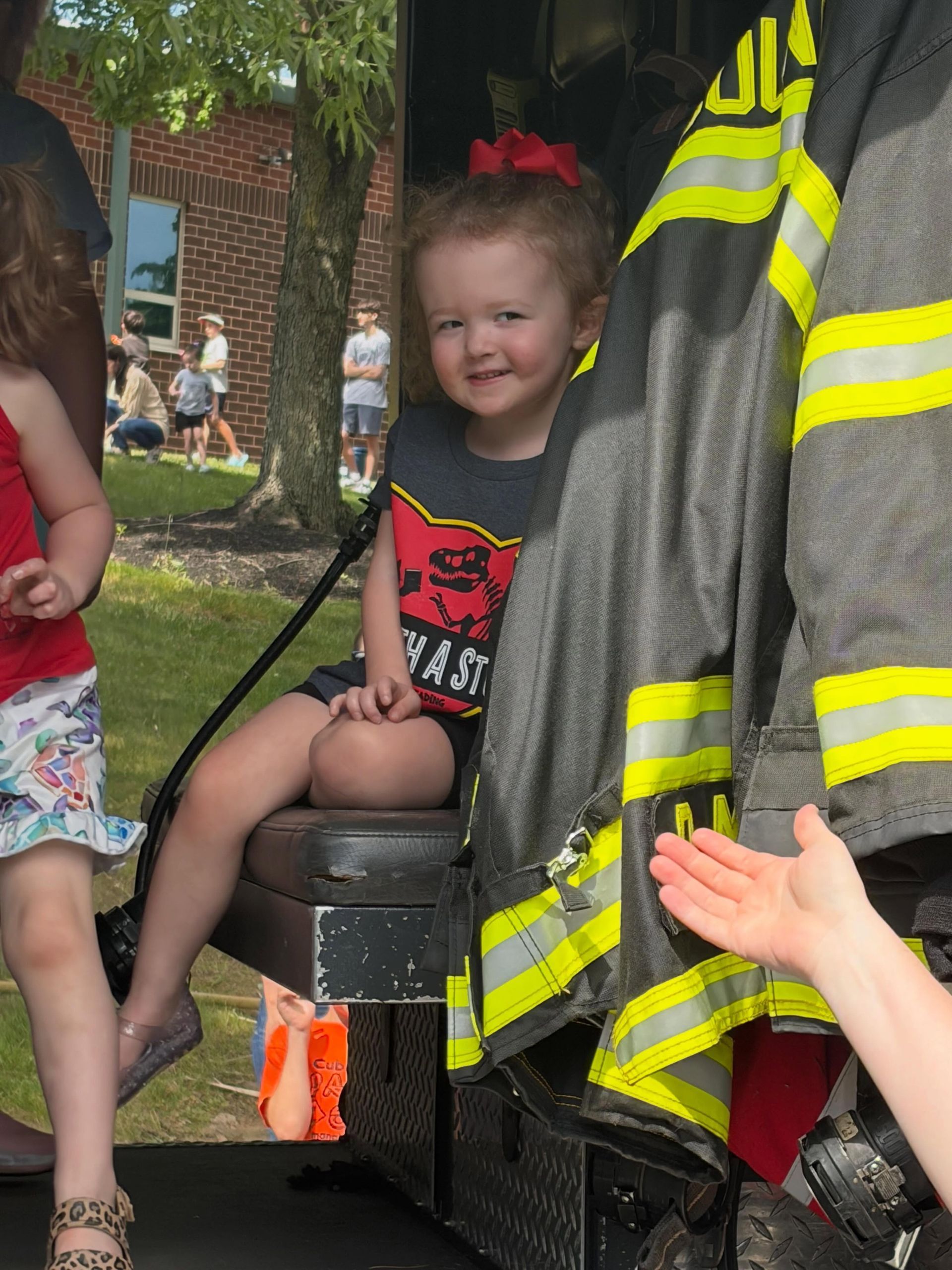 Adley sitting in a fire truck seat beside a firefighter’s reflective jacket at an outdoor event