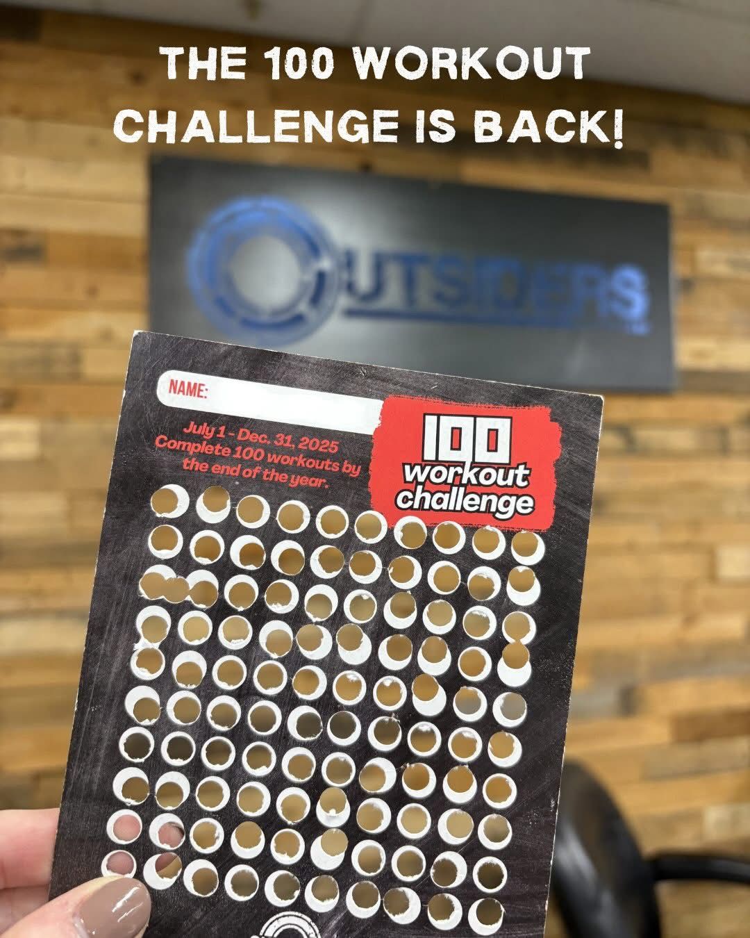 Outsiders CrossFit 100 Workout Challenge punch card held up in front of the gym logo wall in Sparks,