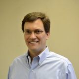 A man wearing glasses and a blue shirt is smiling for the camera.