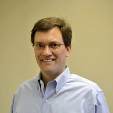 A man wearing glasses and a blue shirt is smiling for the camera.