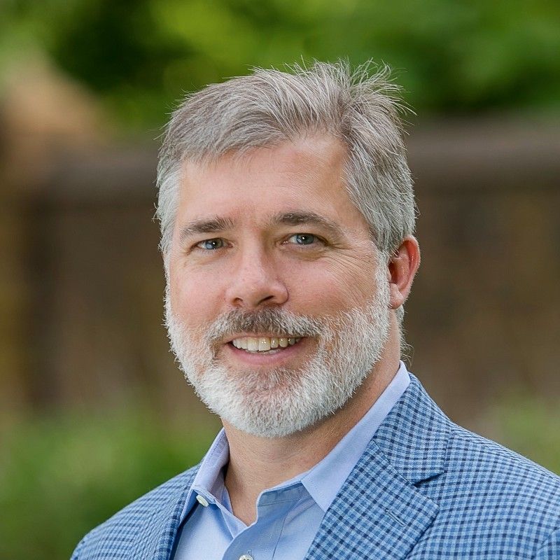 A man with a beard is wearing a blue suit and smiling for the camera.