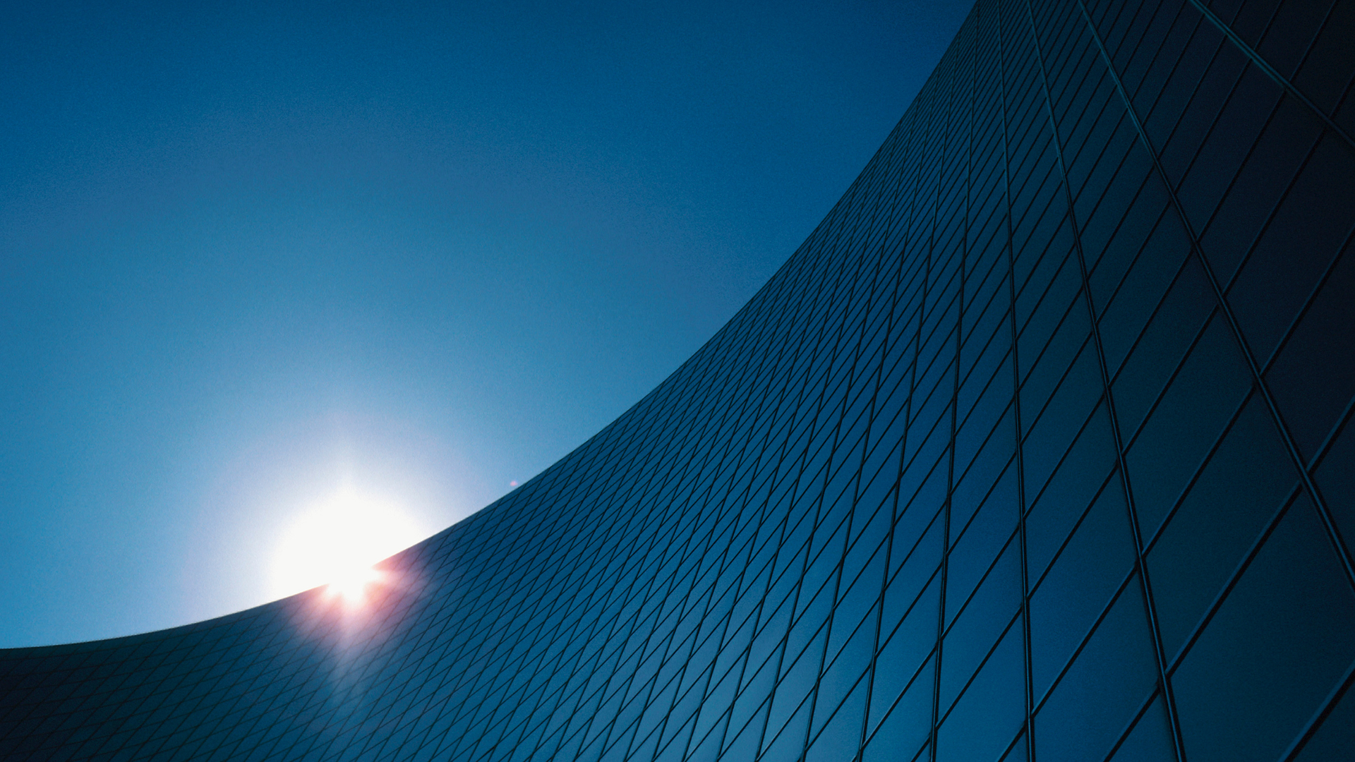 Blue sky and curved glass building facade with the sun glowing at the edge