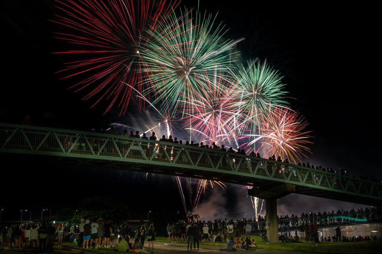 Woman in white uniform smiles, poses outdoors. White top, wrap skirt, green logo.