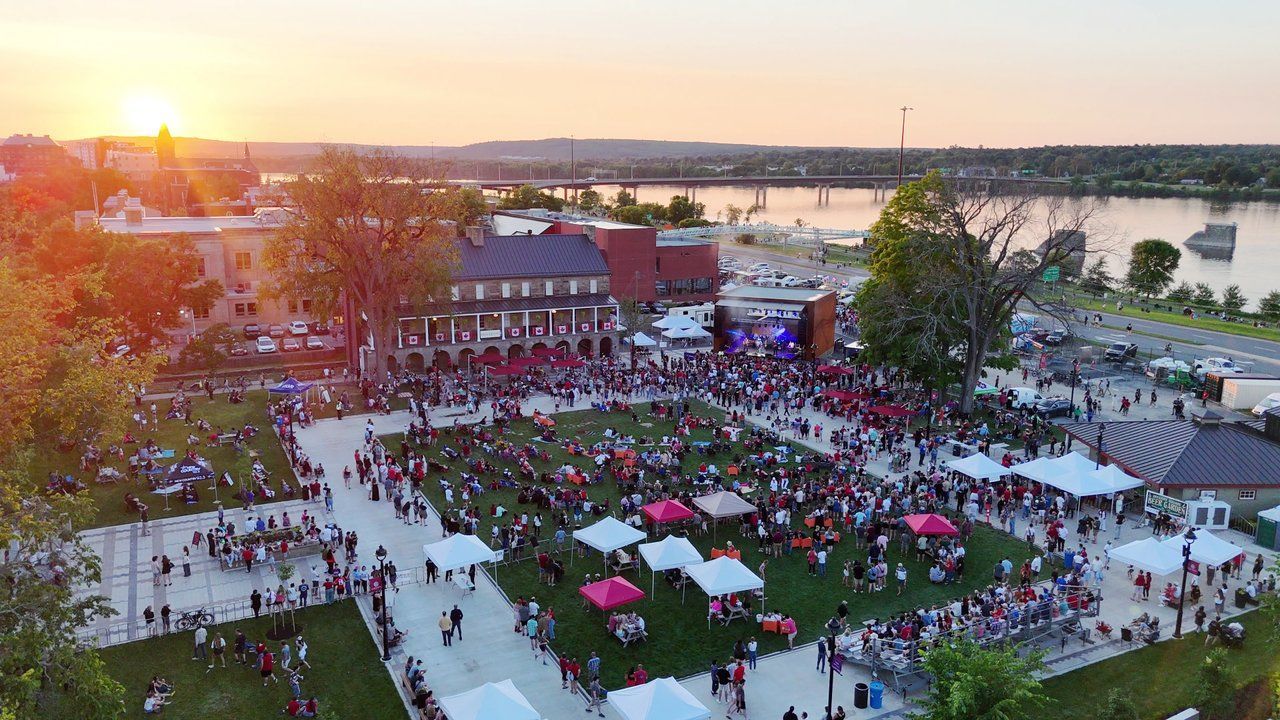 Stage setup at a concert; a person in white pants stands by equipment under the tent-like structure.