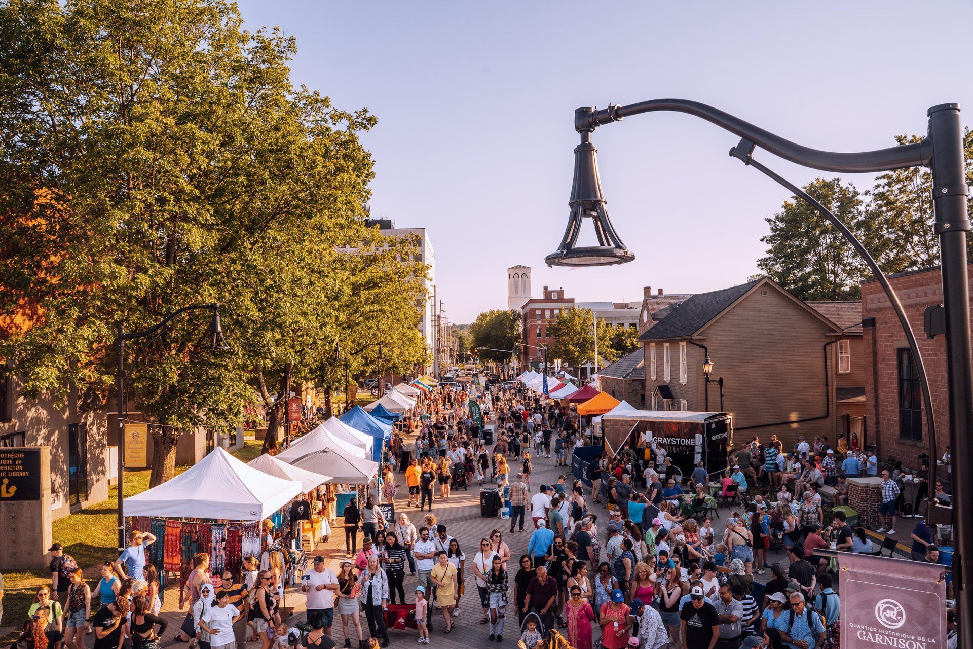 Nighttime outdoor food and drink event with crowds, string lights, tents, and street lights. by Sarah Sarty