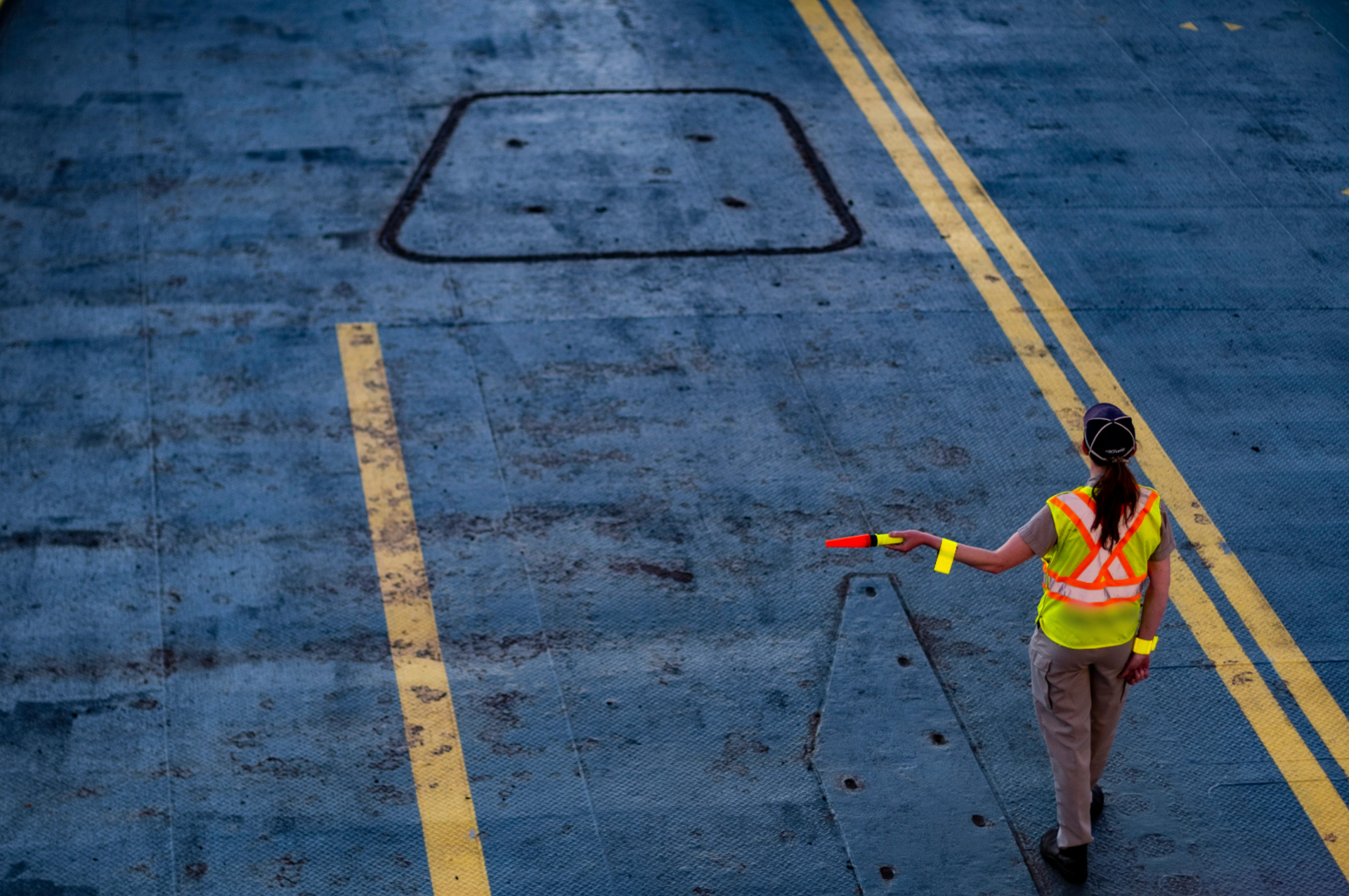 Person in safety vest directs traffic with a wand on a paved surface.