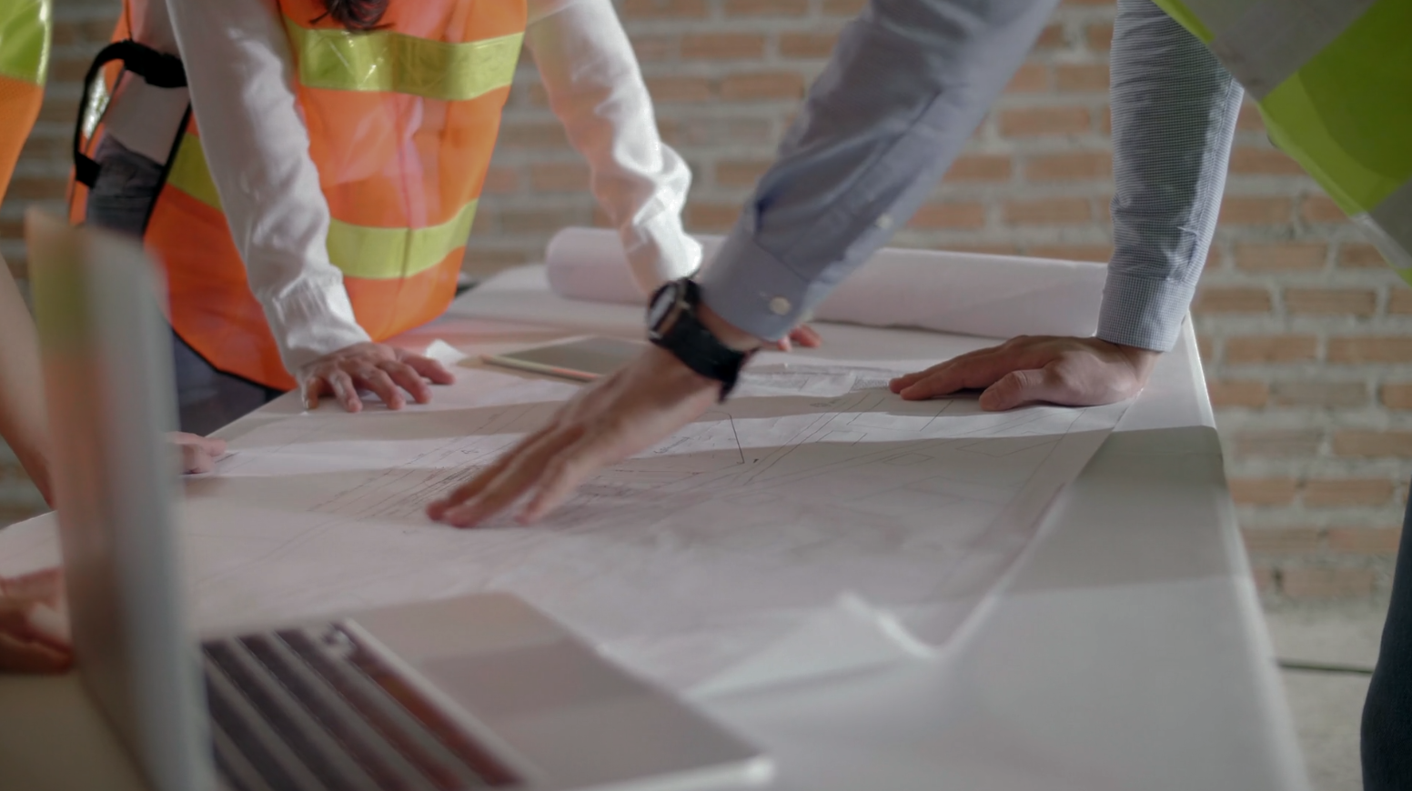 Construction workers examining blueprints on a table, wearing safety vests, indoors.
