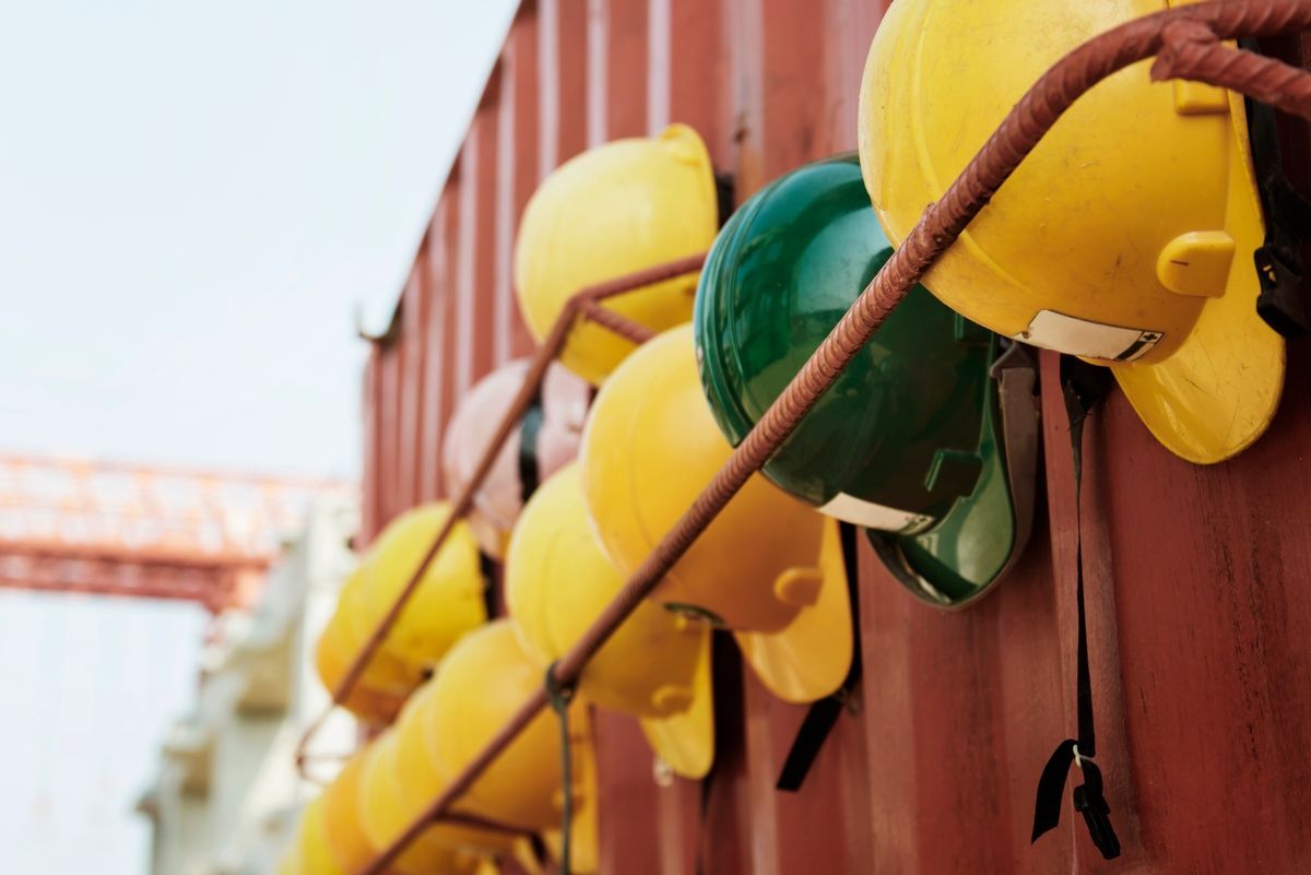 Yellow and green hard hats hanging on a brown metal rack.