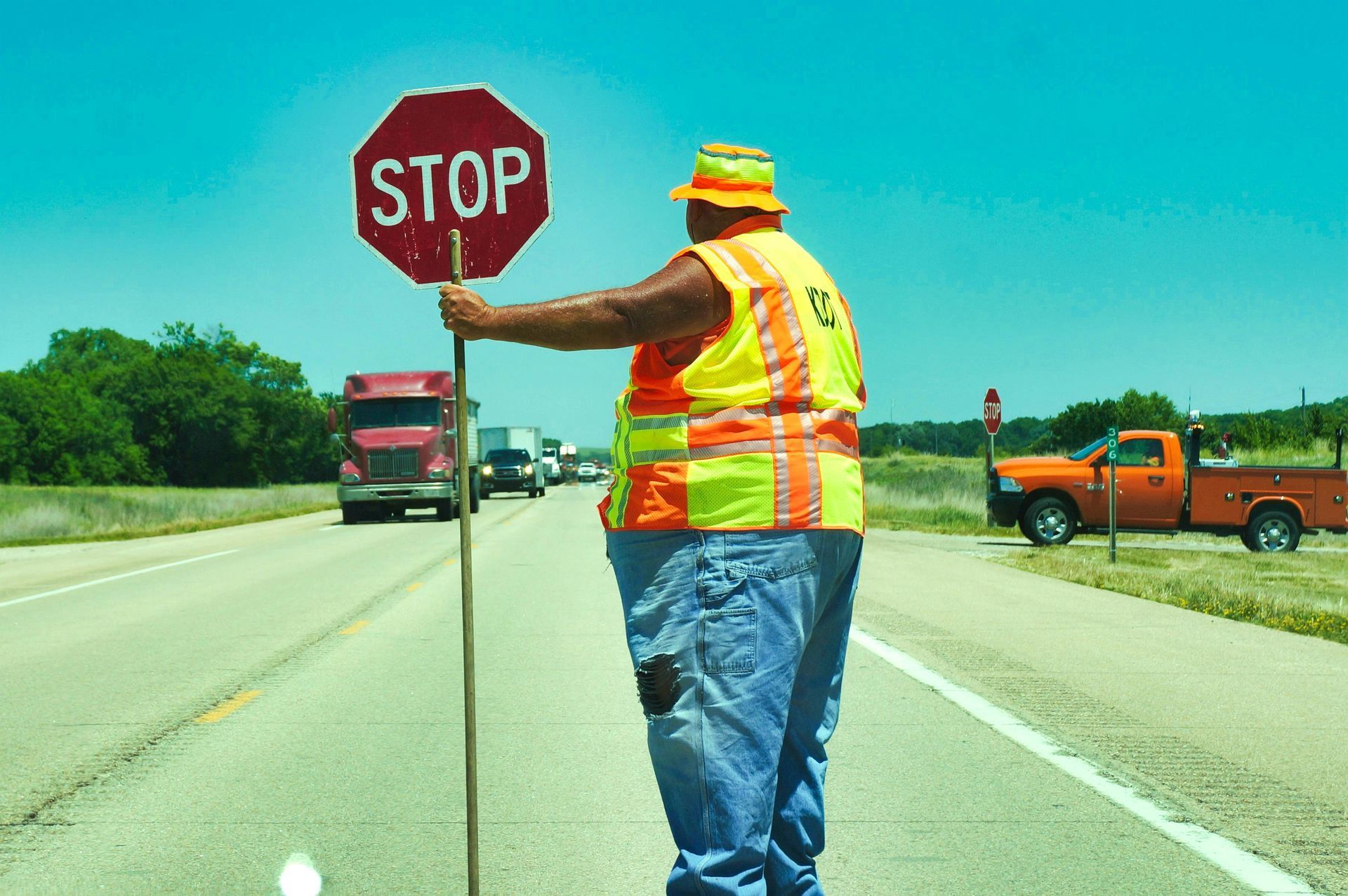 Road worker holding a stop sign, directing traffic on a sunny highway.