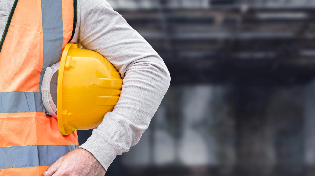 Construction worker holding yellow hard hat, wearing safety vest.