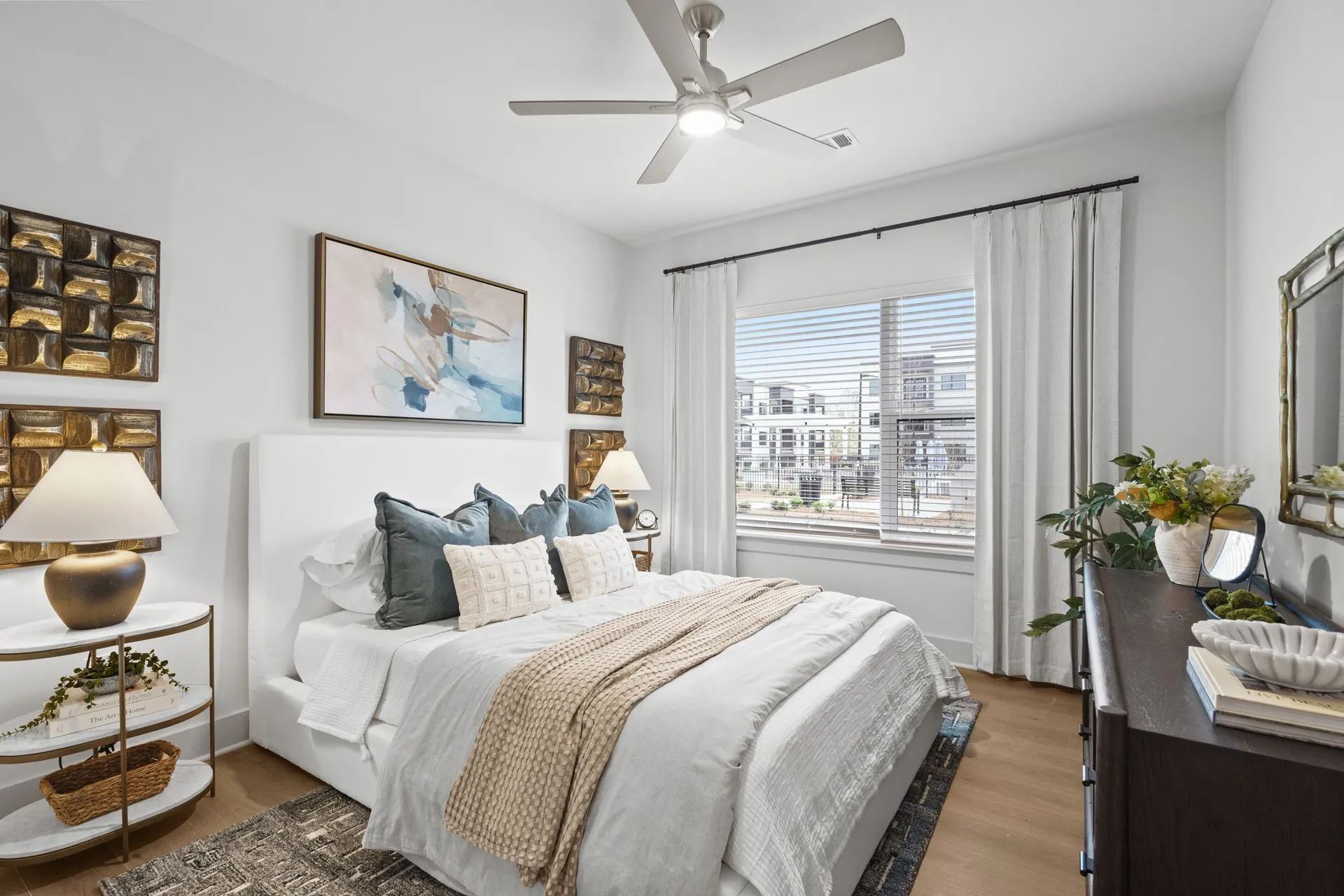 Bedroom with white walls, bed, and natural light, decorated with art and a ceiling fan.