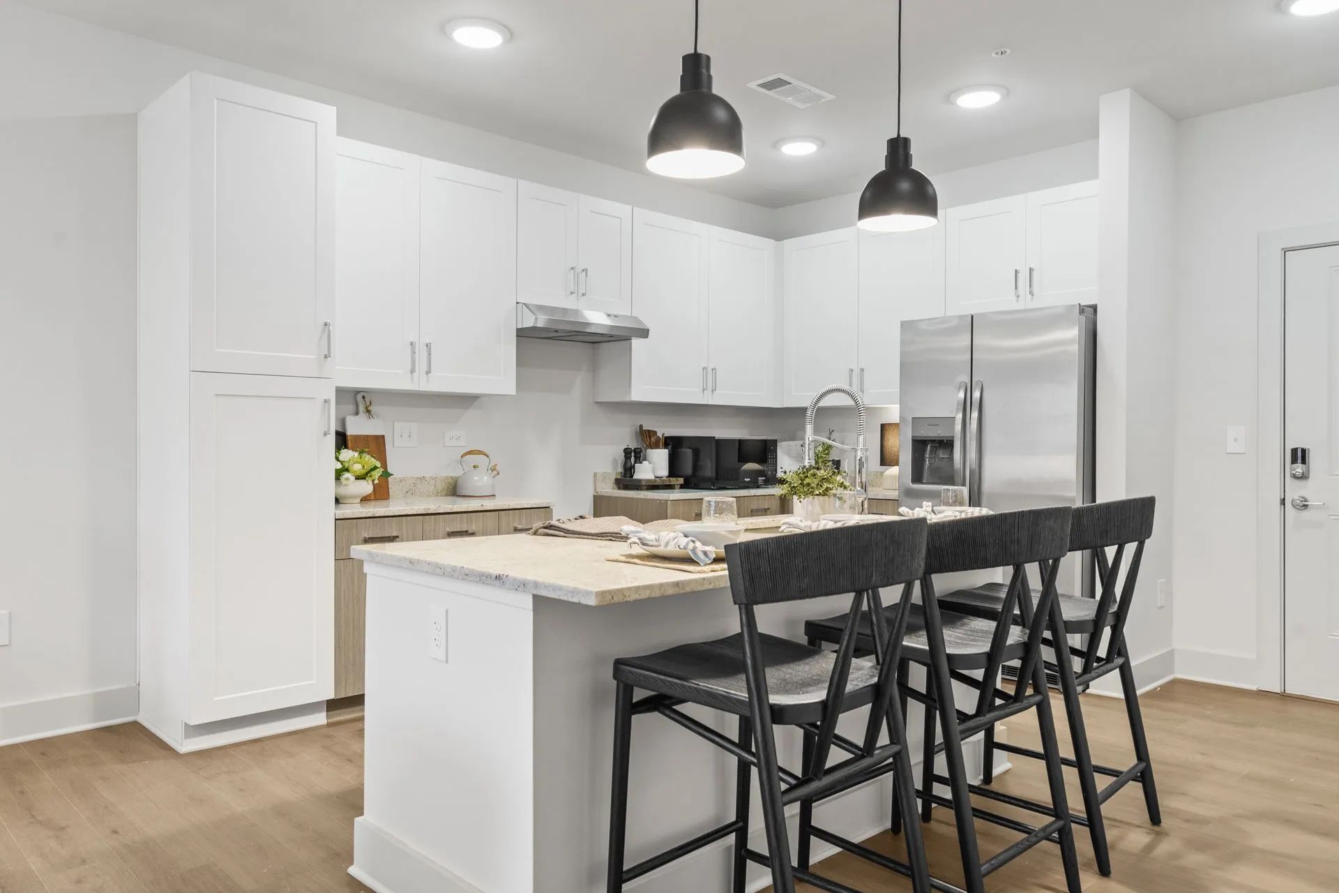 Modern white kitchen with island, black pendant lights, and stainless steel appliances.