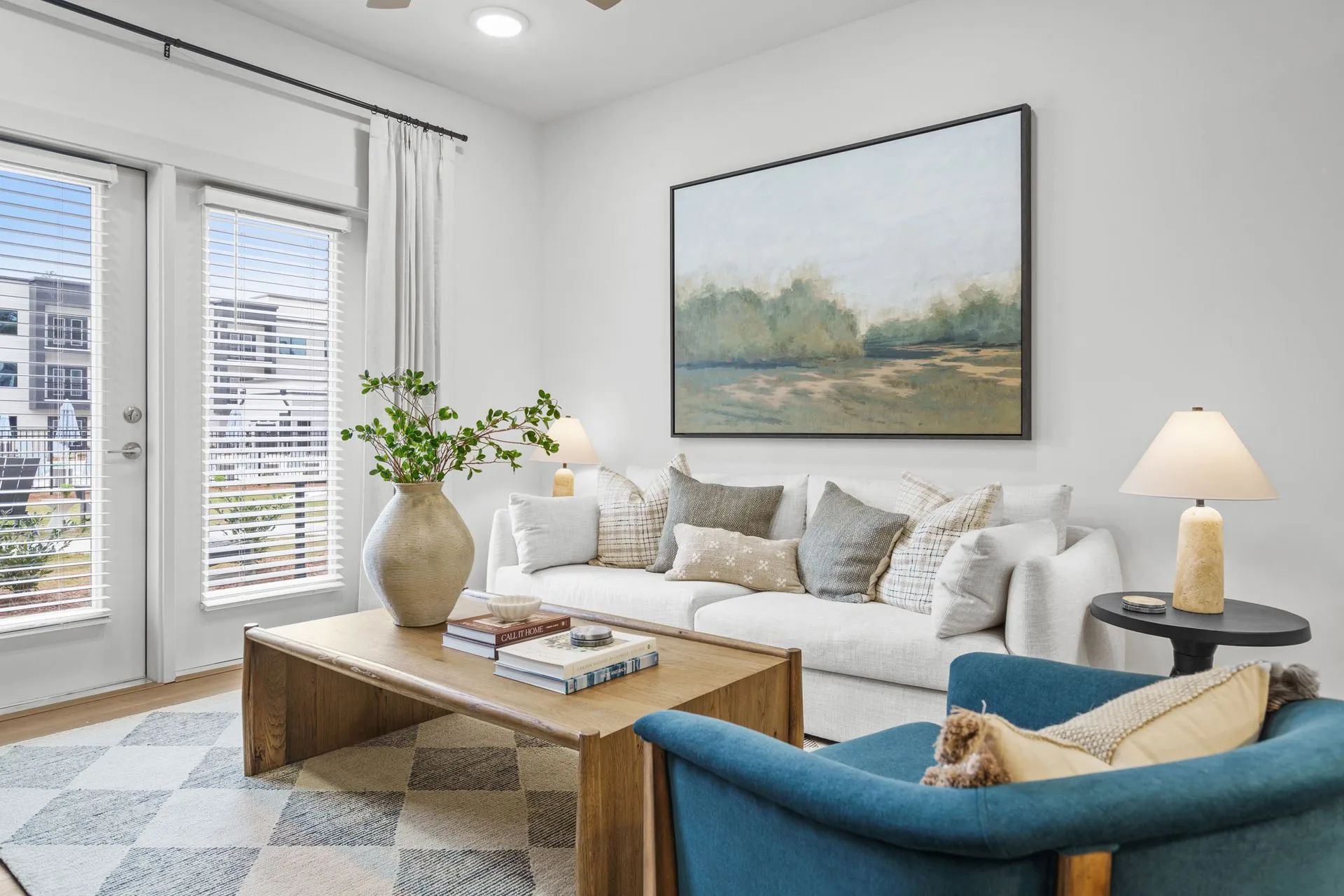 Living room with white sofa, blue armchair, wooden coffee table, and large art piece.