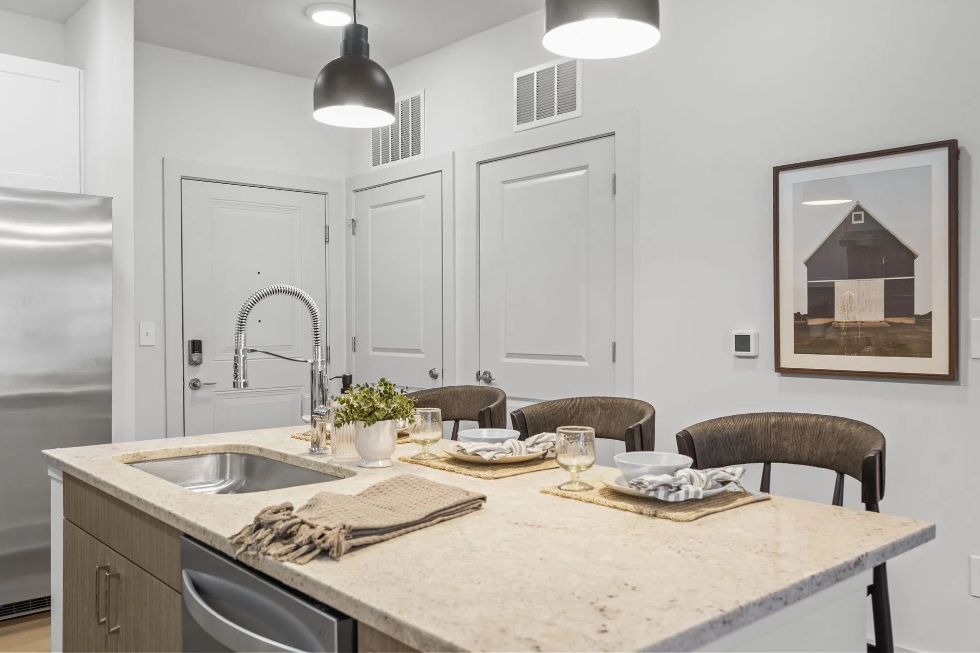 Kitchen with island, sink, stainless steel appliances, two chairs, and a framed art piece.