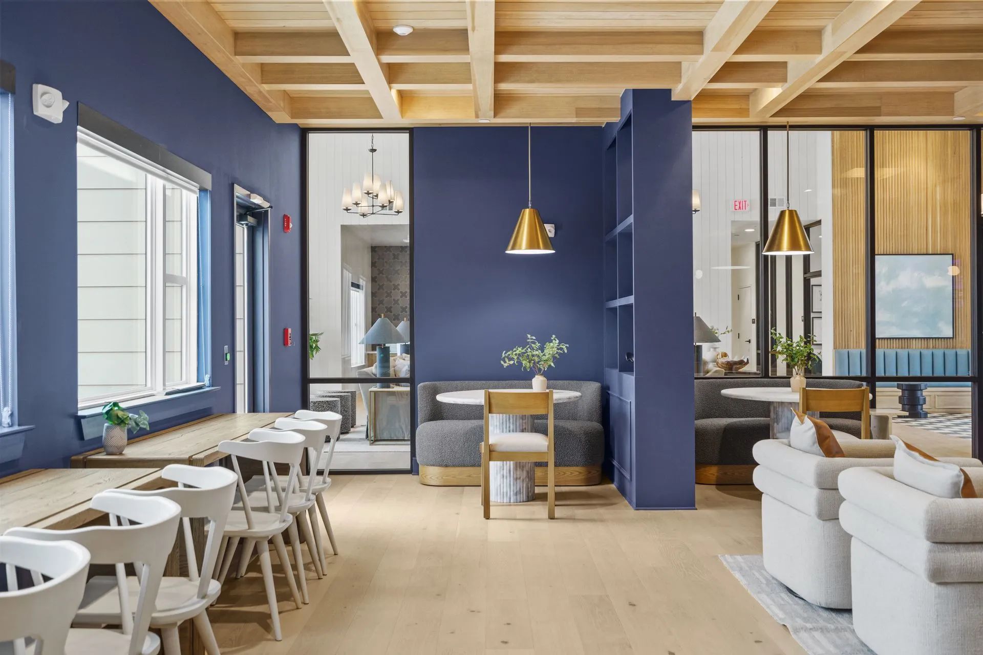 Blue-walled office space with wood ceiling, glass partitions, and seating areas with white chairs and light-colored flooring.
