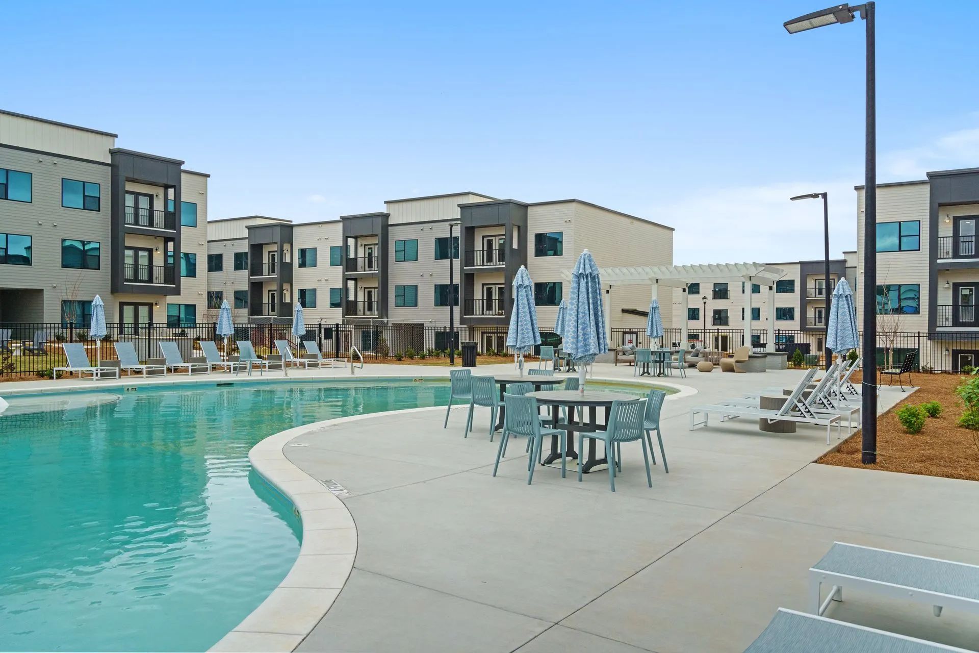 Apartment complex with a pool, patio seating, and umbrellas on a sunny day.