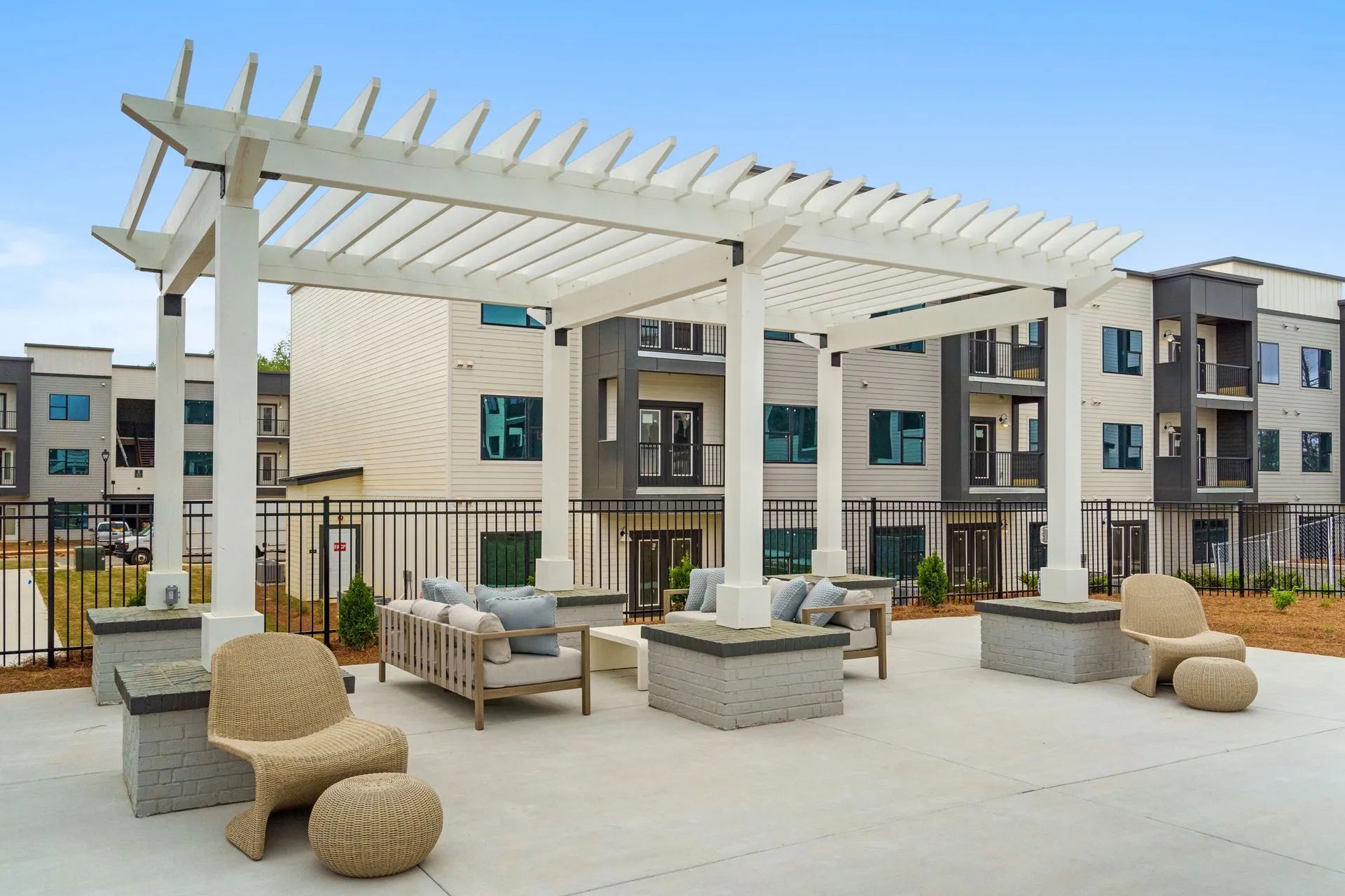Outdoor seating area under a white pergola. Modern apartments in the background.