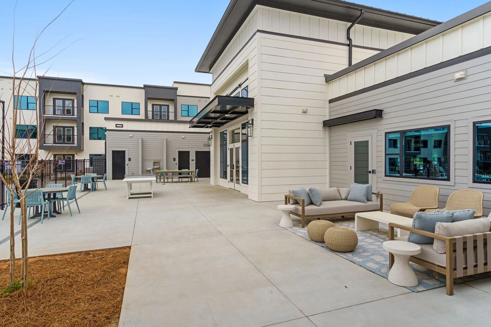 Outdoor patio with seating: couches, chairs, tables. Beige building, blue accents, overcast sky.