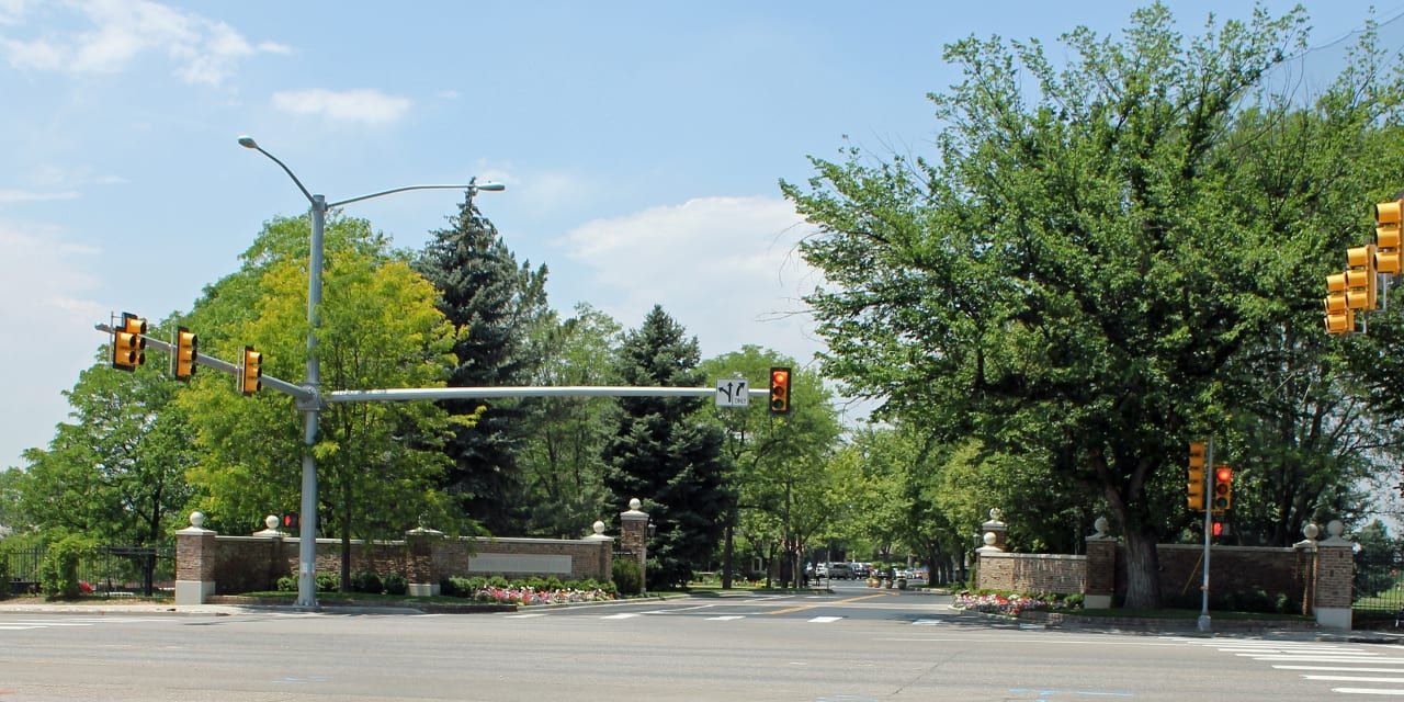 Entrance with brick pillars, green trees, traffic lights, and a clear blue sky.
