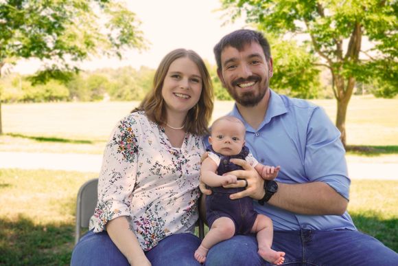 A man and a woman are holding a baby in a park.