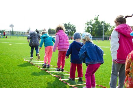 Children in colorful jackets walking on a grassy field with a rope line outdoors