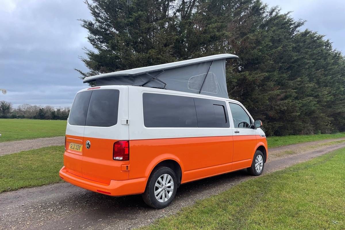 An orange and white van with a pop up roof is parked on the side of a road.