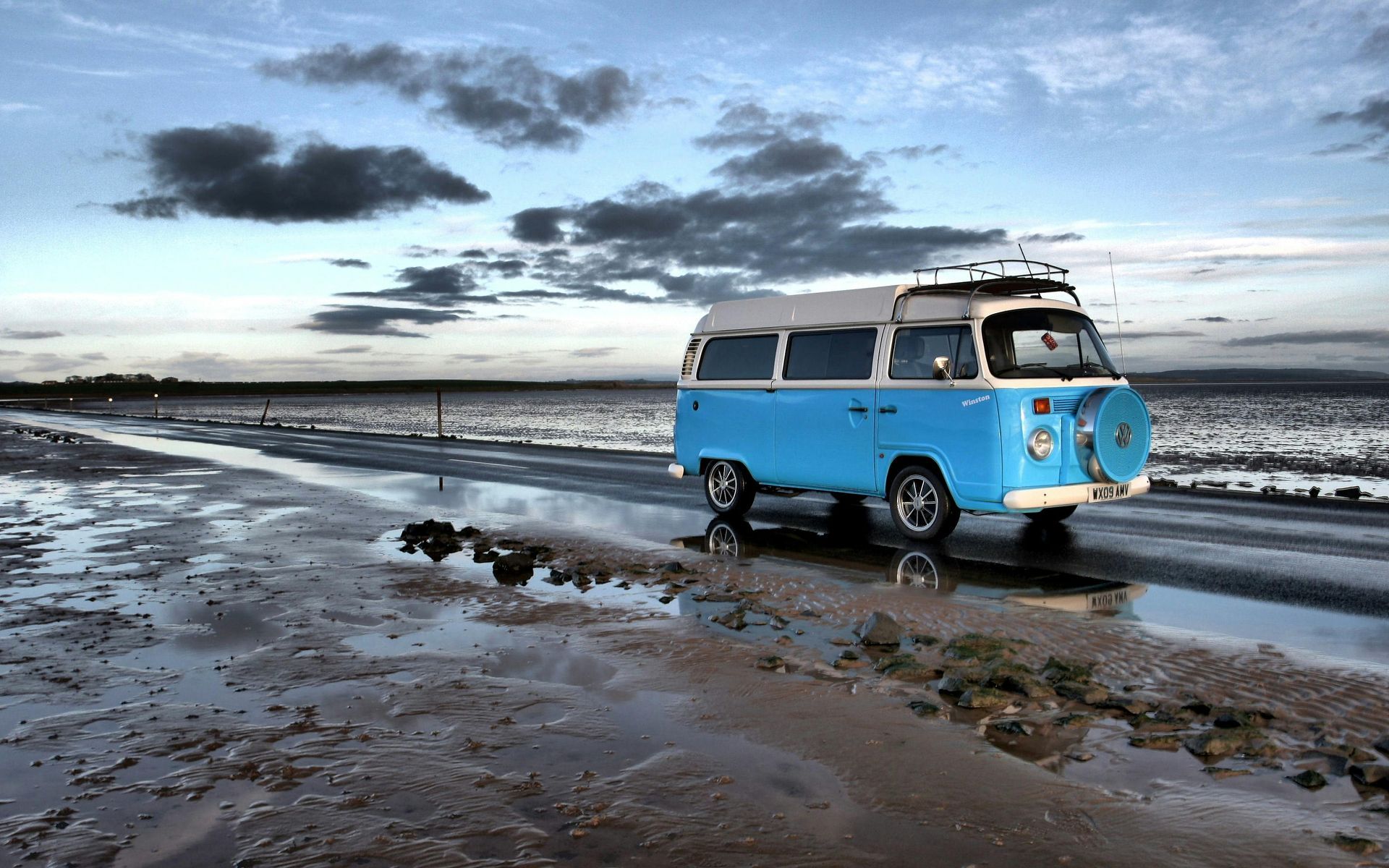 A blue campervan is parked on the beach near the ocean. ready for campervan hire in the UK