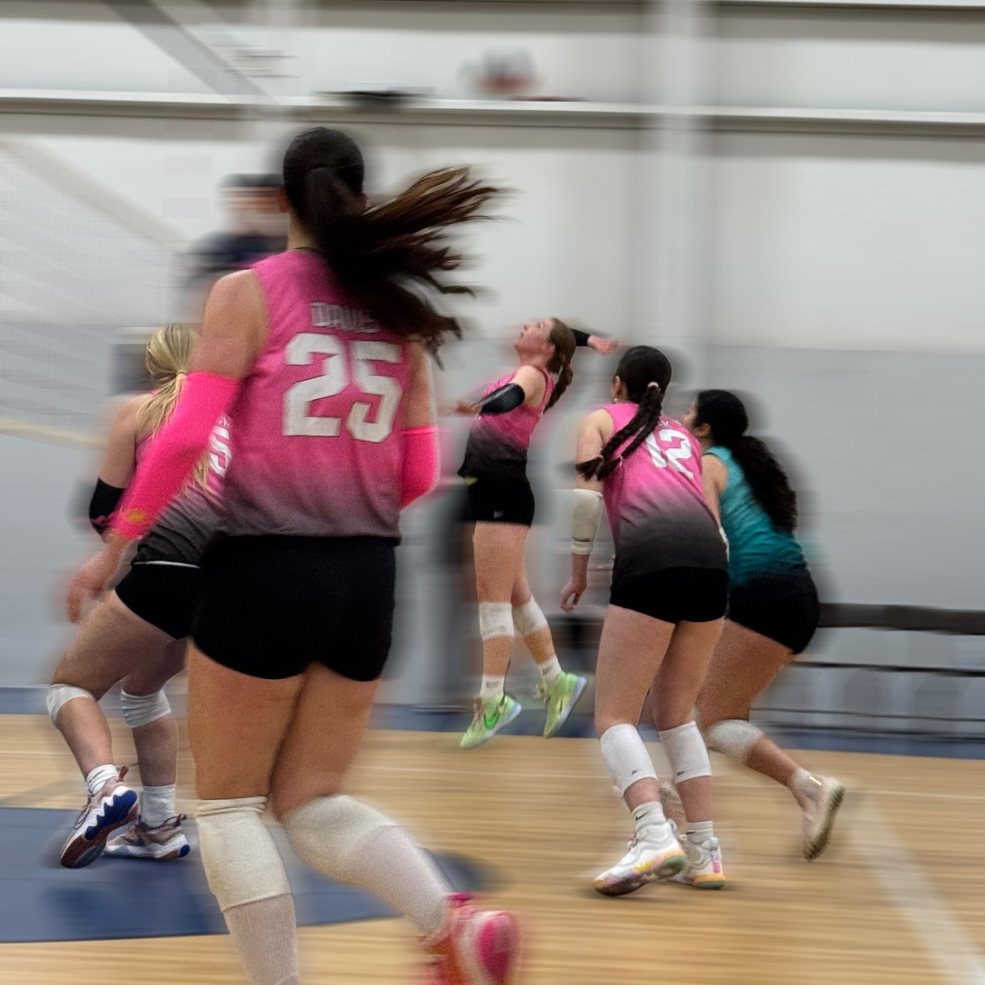 Volleyball players in pink and black uniforms moving on a gym court during a match.