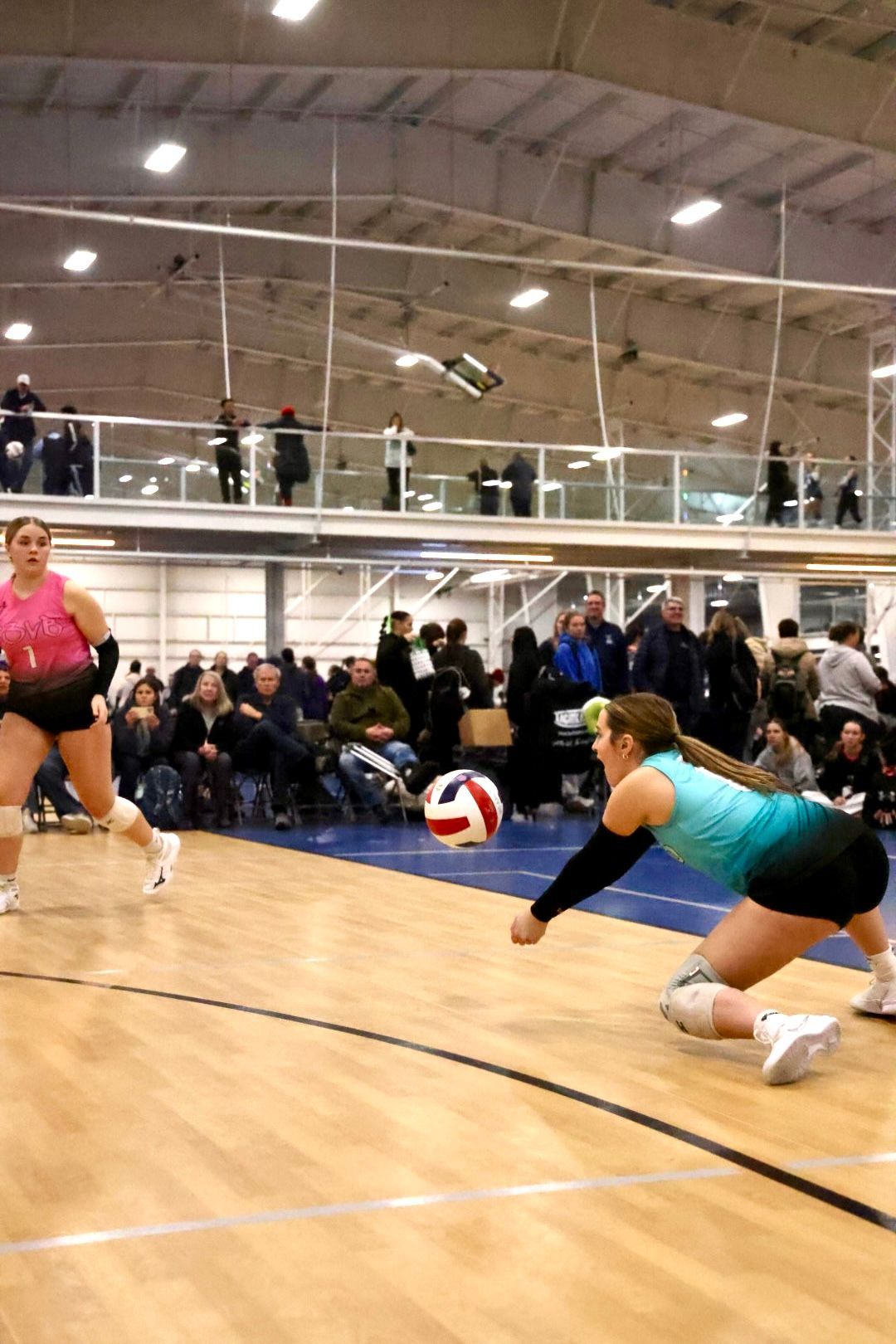Volleyball player diving to hit the ball during a game in a gym with spectators.
