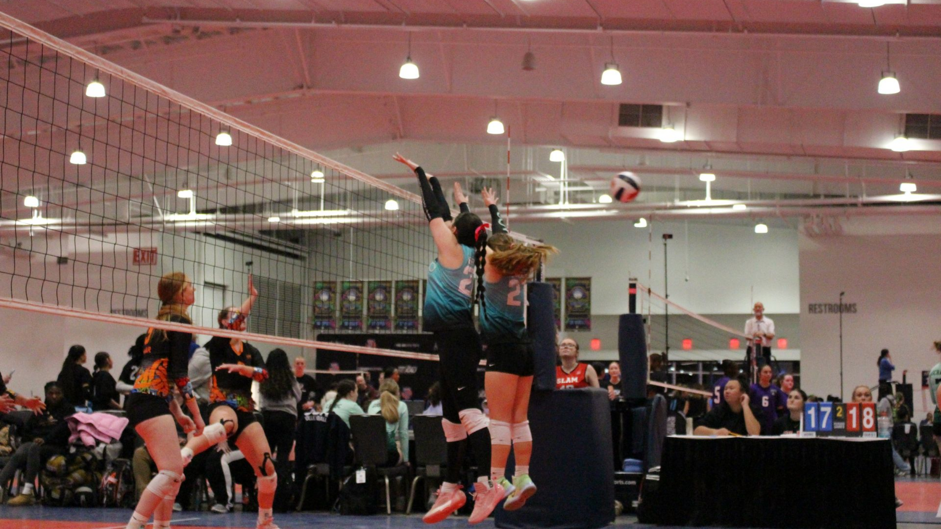 Volleyball players jumping to block a ball over the net in a sports arena.