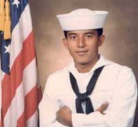 A man in a sailor 's uniform is standing in front of an american flag.