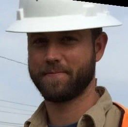 A man with a beard wearing a hard hat and an orange vest.