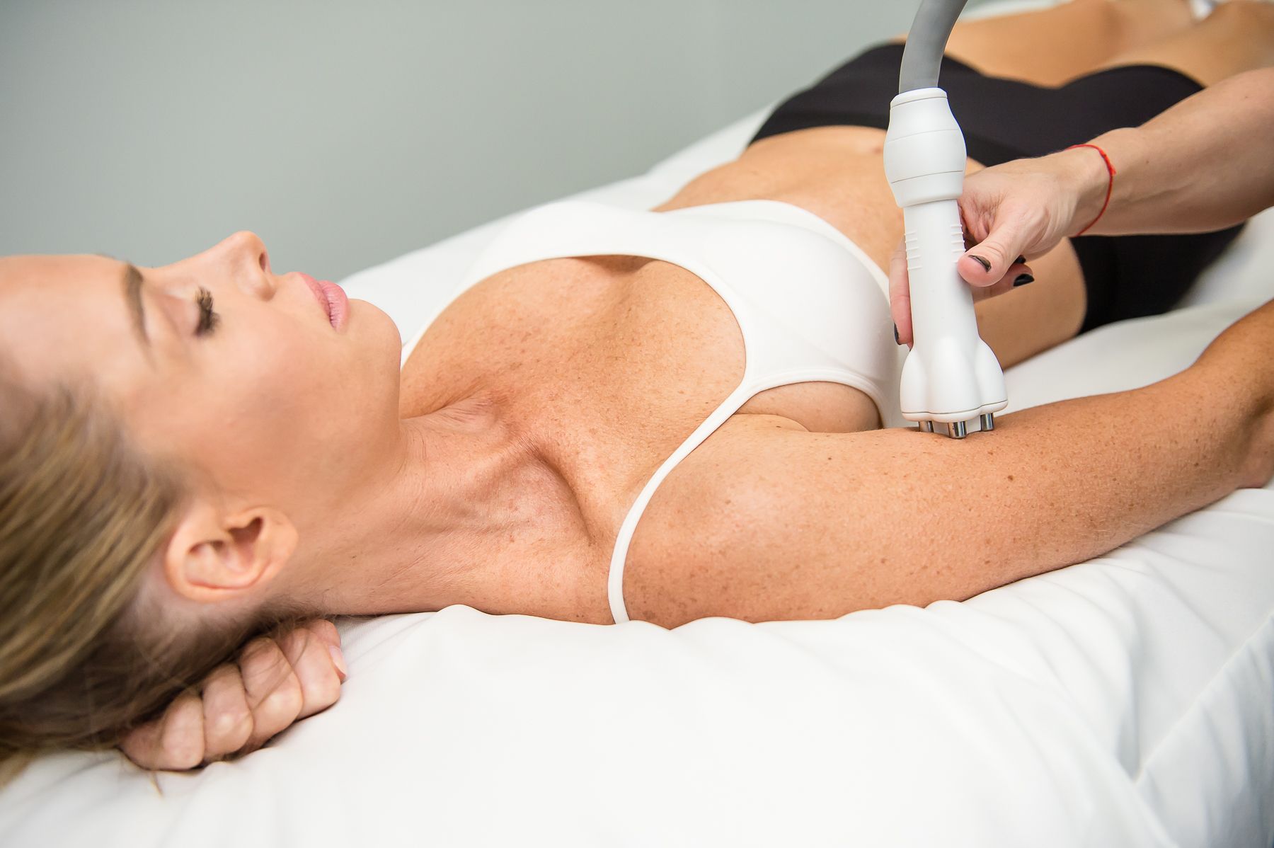Woman receiving arm treatment on a medical bed. Technician uses a device, focused expression.