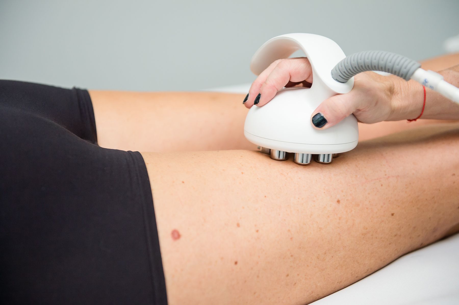 Person receiving body sculpting treatment on their leg with a white handheld device.
