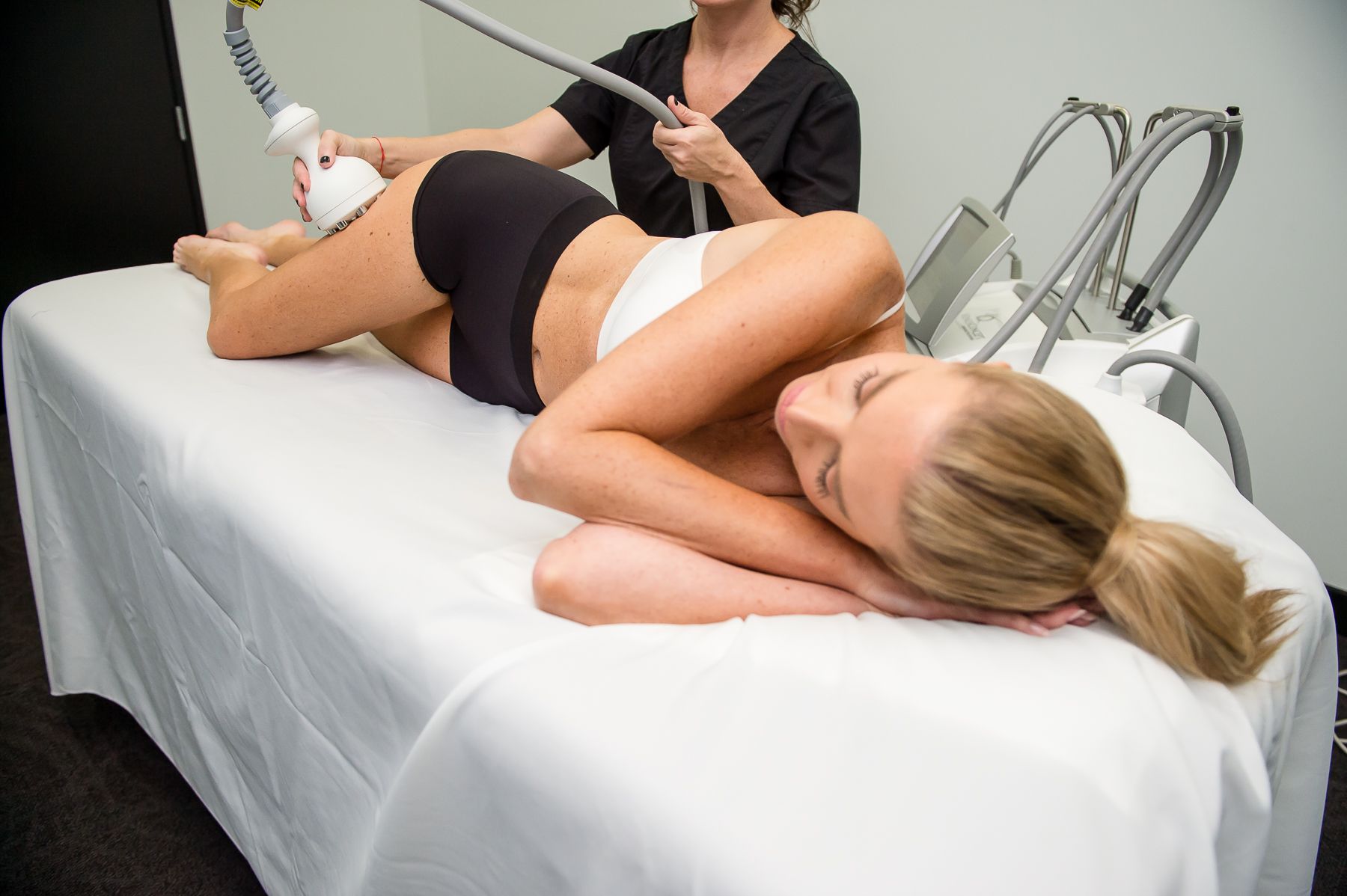 Woman receiving body contouring treatment on her buttocks. A technician uses a device in a clinic.