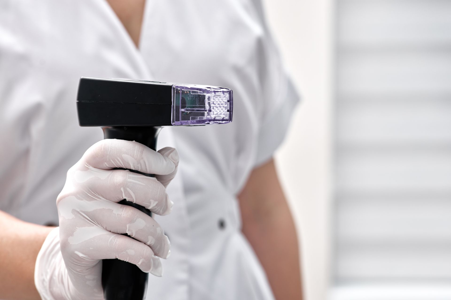 Gloved hand holding a handheld digital thermometer against a white background